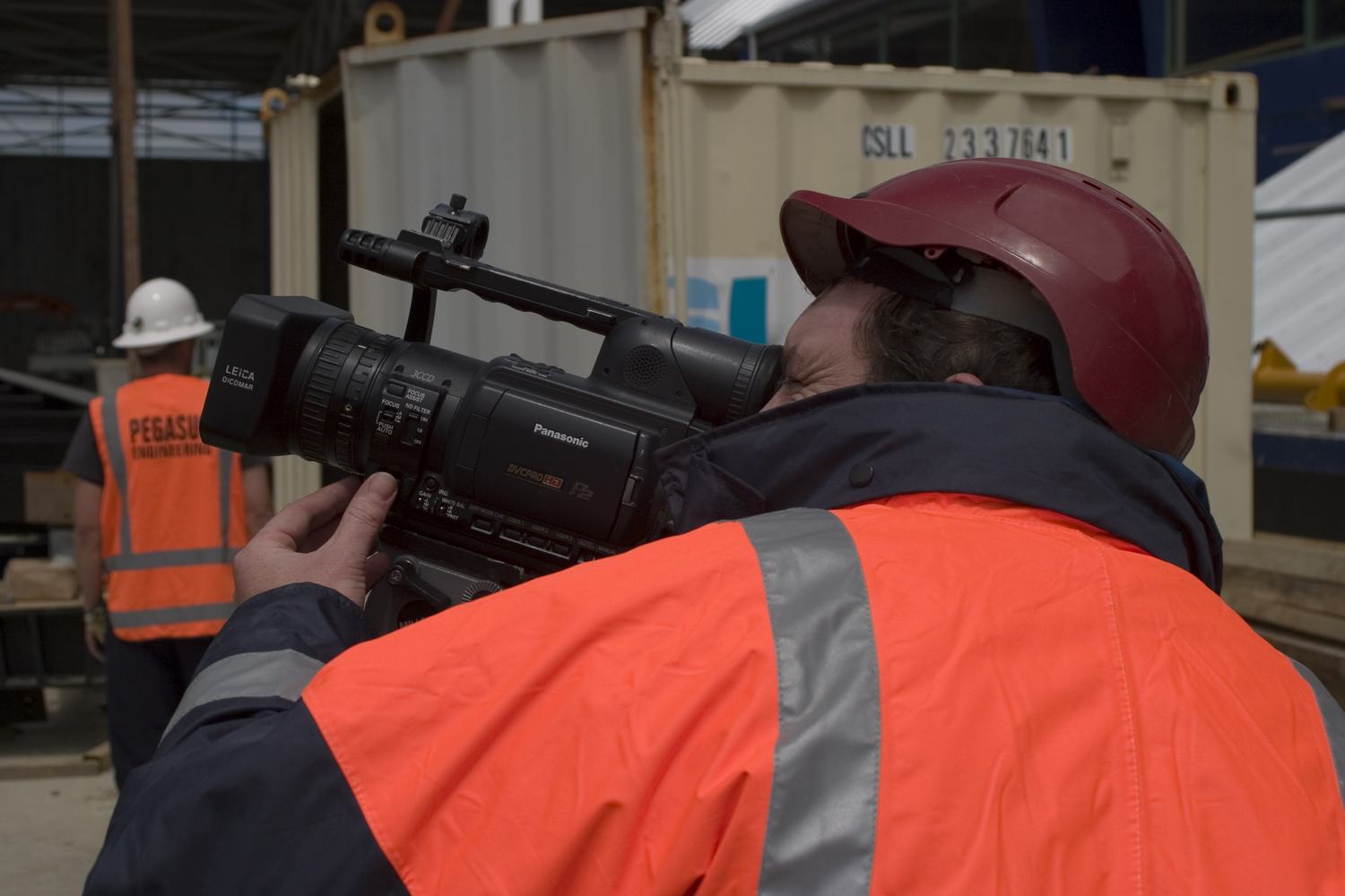 A camera operator in a high-visibility jacket filming