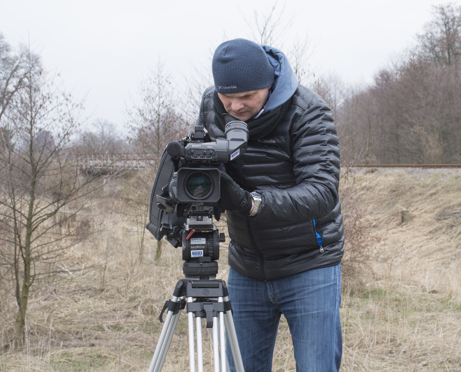 A cameraman filming in the field on a tripod